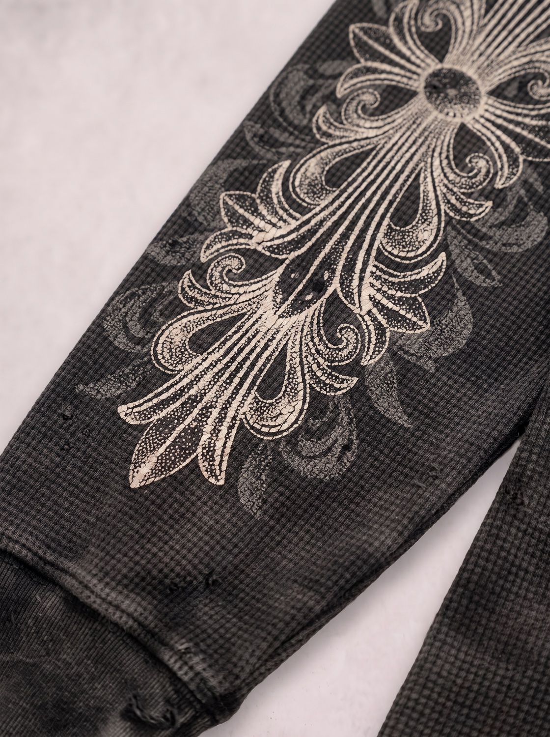 Macro detail of the sleeve filigree, ink cracked and sunk into the waffle knit