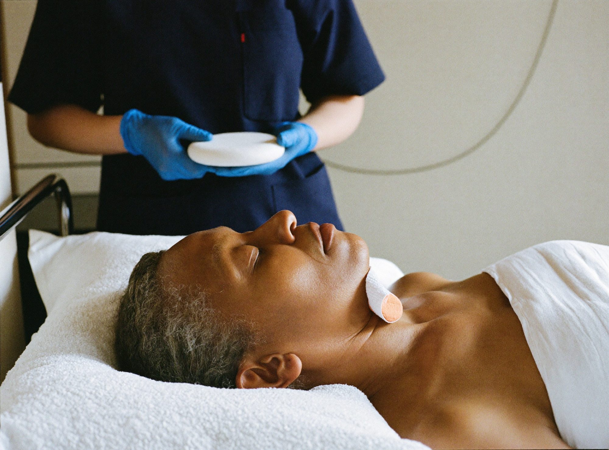 A nurse in blue gloves cleansing a woman's jawline before treatment