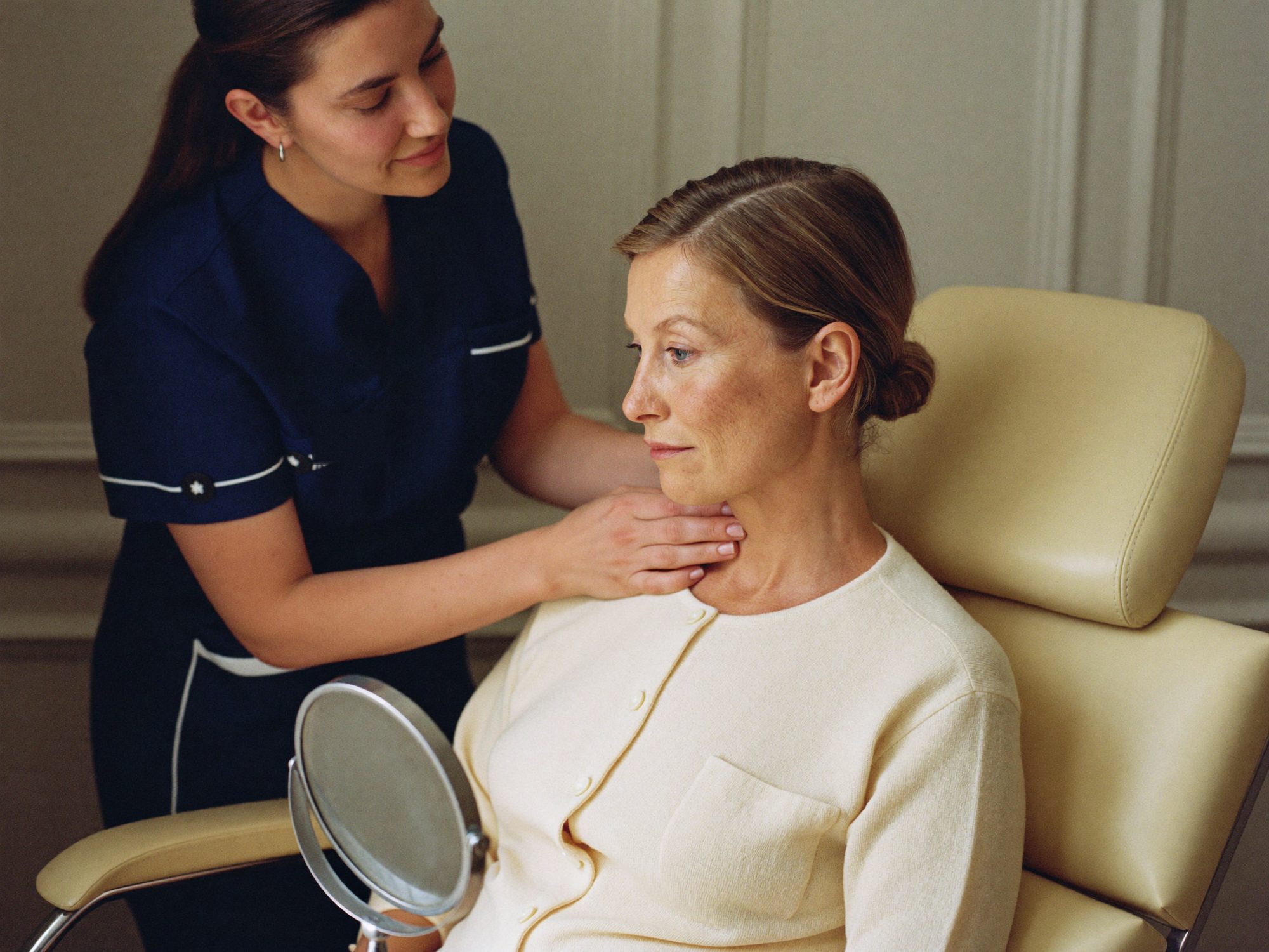 A doctor in navy scrubs talking a seated patient through her cheekbones and jawline