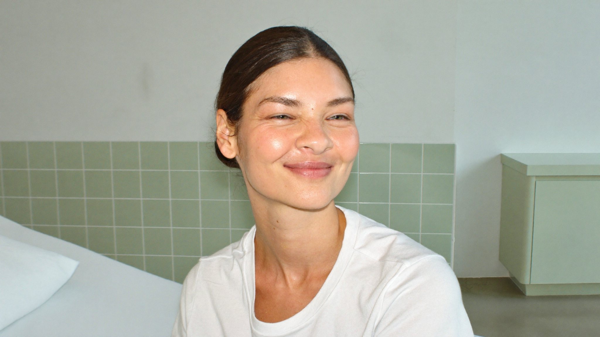 A smiling Patch client sitting on a treatment bed in front of sage green tiles