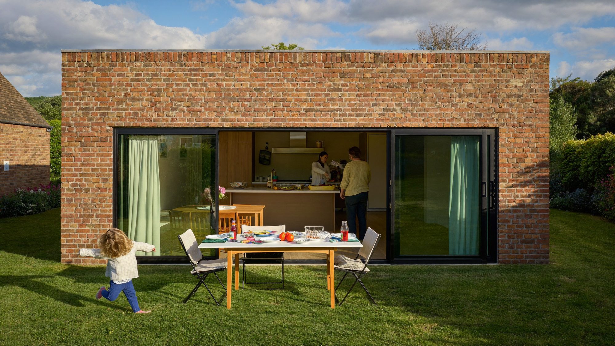 A brick single-storey rear extension with sliding doors open to the garden, a child running on the lawn