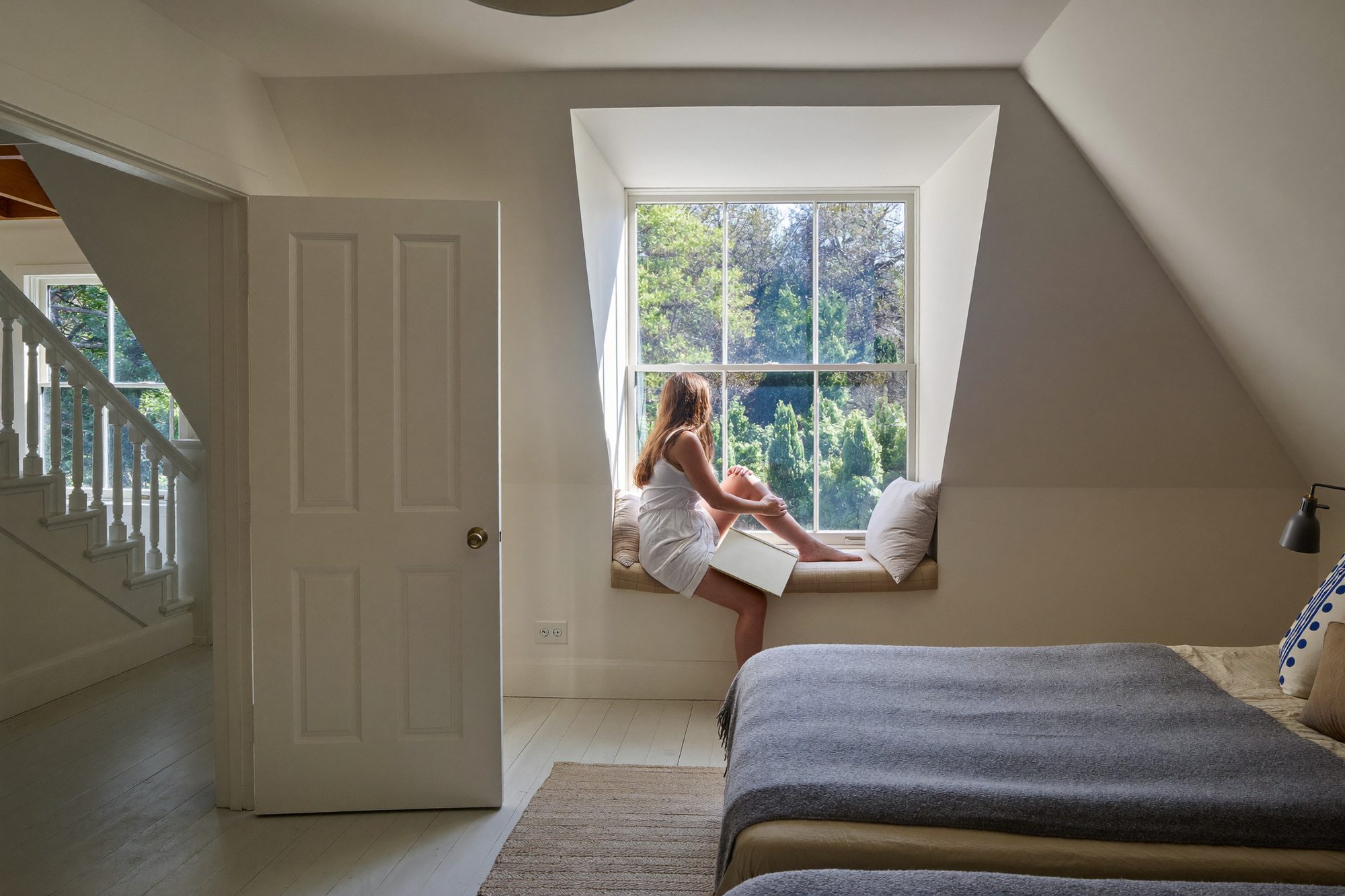 A finished loft bedroom with a dormer window seat, a girl reading by the window