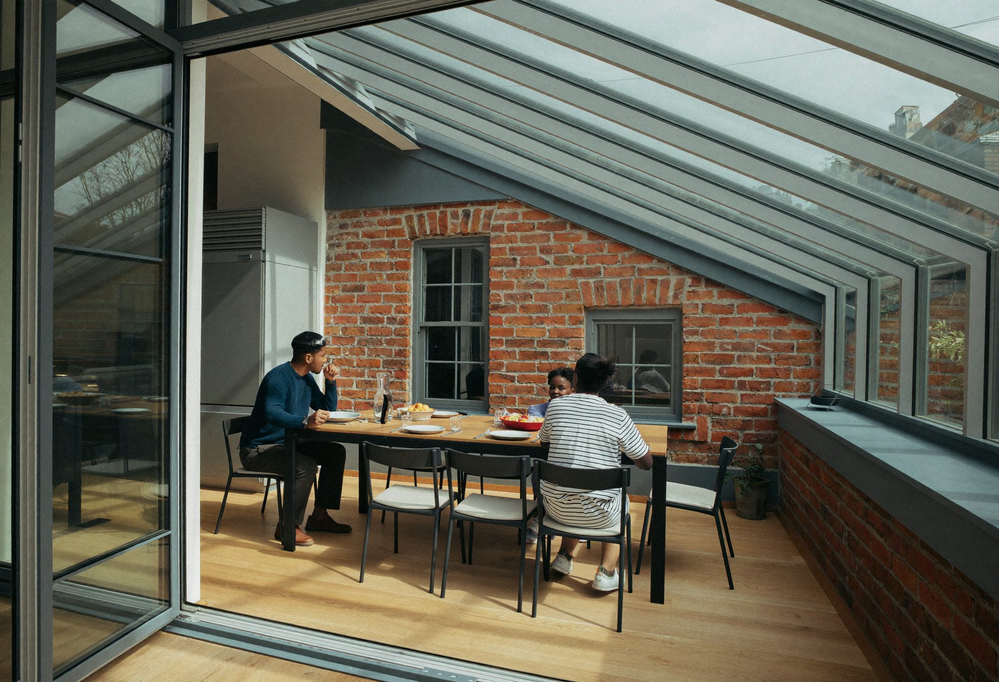 A Victorian terrace kitchen opened into a glazed side return against red brick, a family at the table