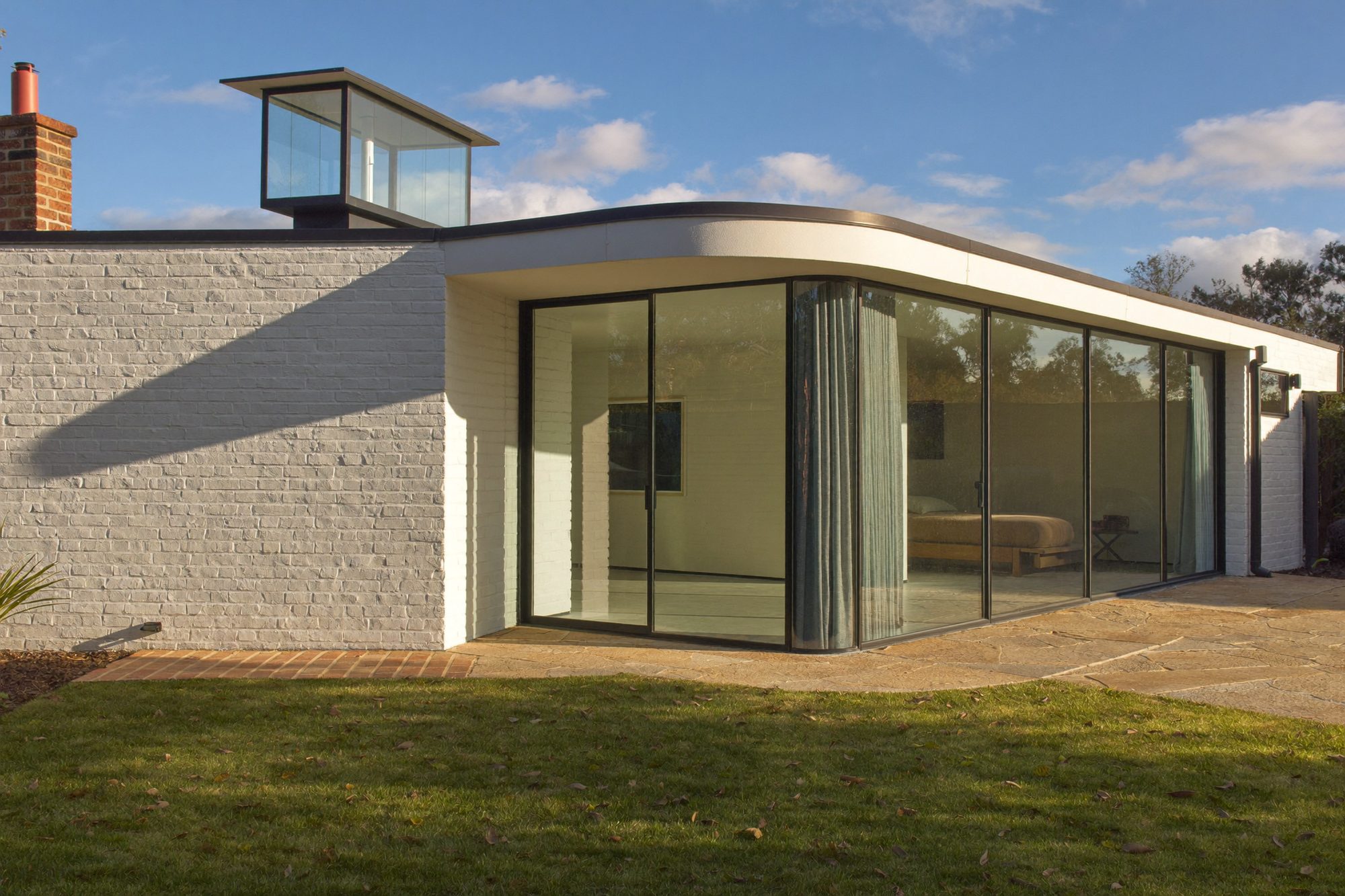 A white-brick wrap-around extension with corner glazing and a roof lantern, seen from the garden